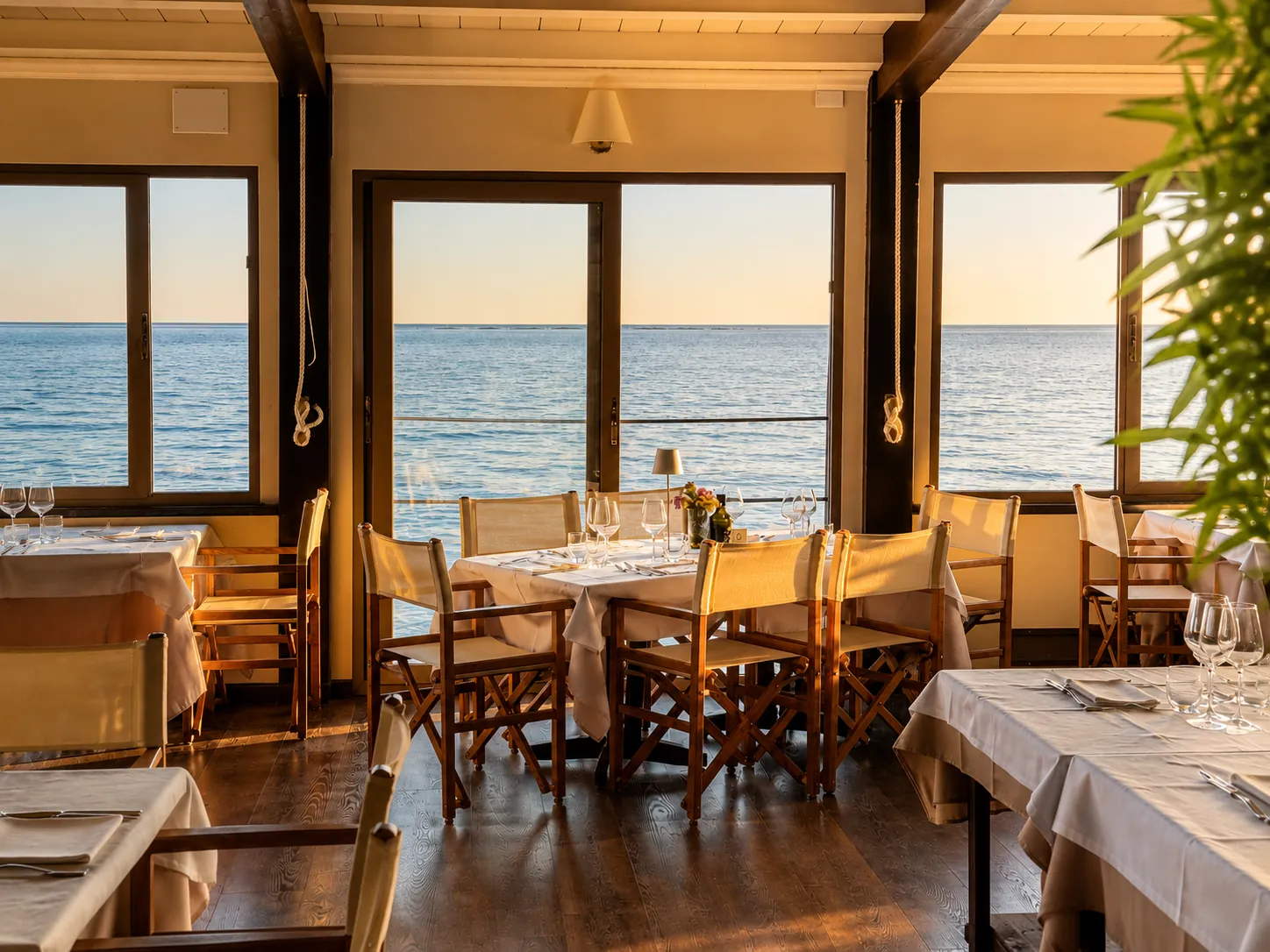Sala del ristorante Bagni Serenella illuminata dal tramonto con tavoli vista mare